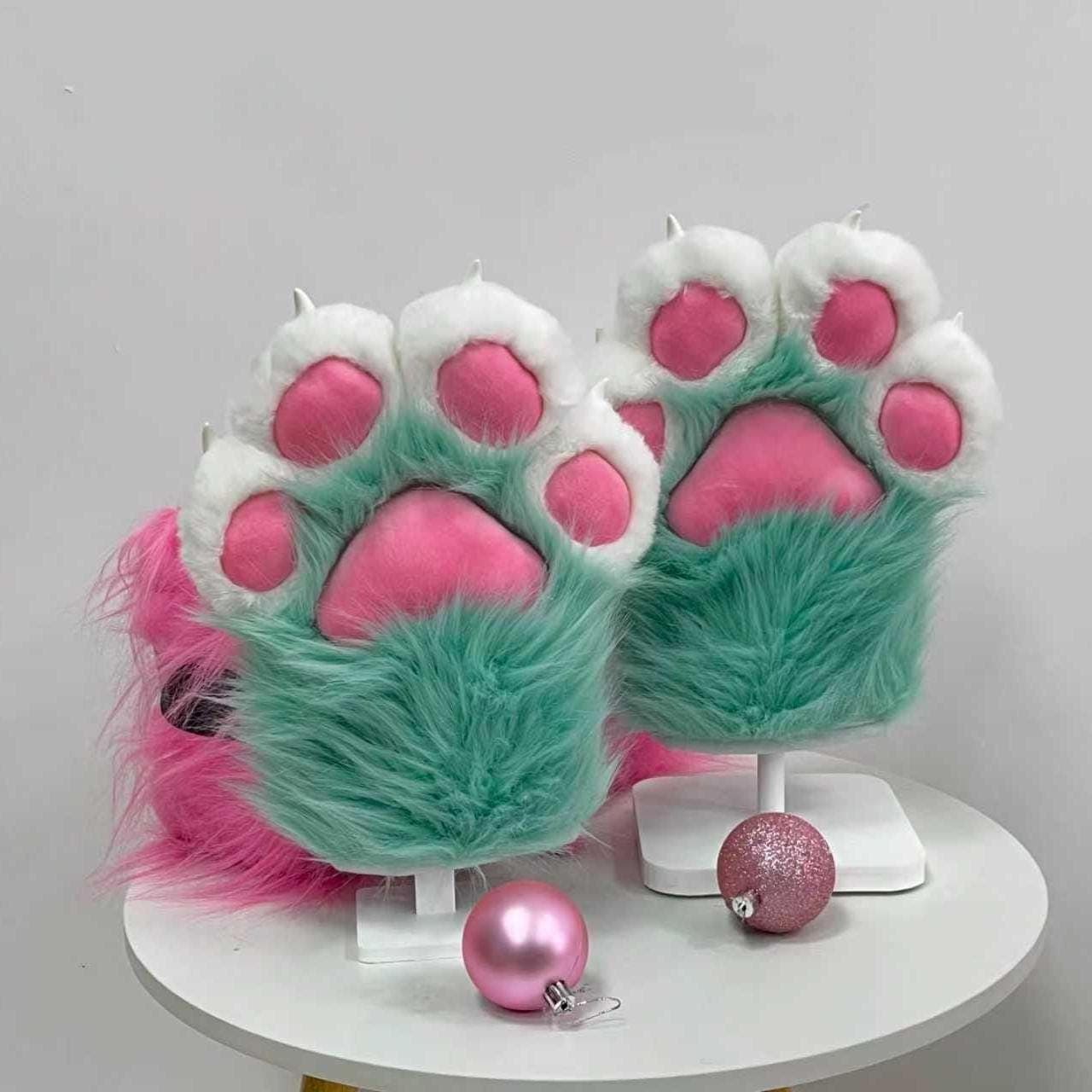 Seafoam teal furry handpaws front angle showing four puffy fingertip pads and a giant center bean stuffed in vivid hot pink minky fabric. The long pile faux fur gives a candy soft pastel vibe perfect for toony fursona looks, protogen builds or partial kigu cosplay. Stuffed puffy beans add that plushie sculpted silhouette loved across the furry fandom. Easy slip on mitten paws for pop culture cons, furcon, rave nights, cosplay skits and fursuit walks with total comfort and cute factor.