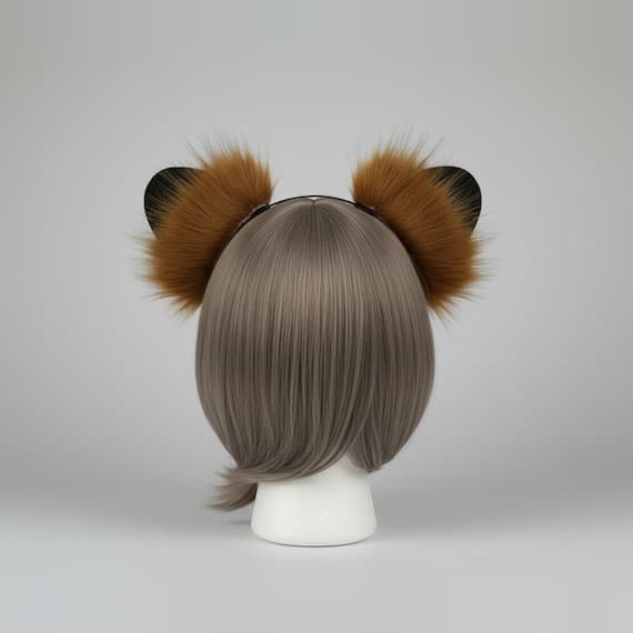 Rear view of tiger beast ear headband showing long fluffy wispy tawny golden-brown faux fur on ear backs radiating outward with black border edges visible and slim black metal headband on a mannequin head with grey-brown bob wig, back view tiger ears cosplay furry ears costume ears beast ears animal ears headband faux fur ears cosplay animal ears fluffy ears fantasy ears tiger ears headband cosplay headband animal cosplay against neutral grey studio background
