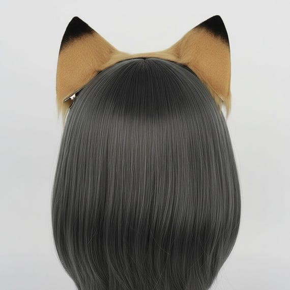 Rear view of tawny brown faux fur lion ear hair clips shown from back of mannequin head with cool dark grey bob wig. Both clip on lion ears visible from behind clipped securely into hair. Ears show tawny brown fluffy fur with black tipped edges demonstrating how clip on ears look when worn from back angle. Animal costume safari outfit animal accessories kids dress up stage costume performance theatrical costume dress up accessories party animal. Studio product photo on neutral grey background.