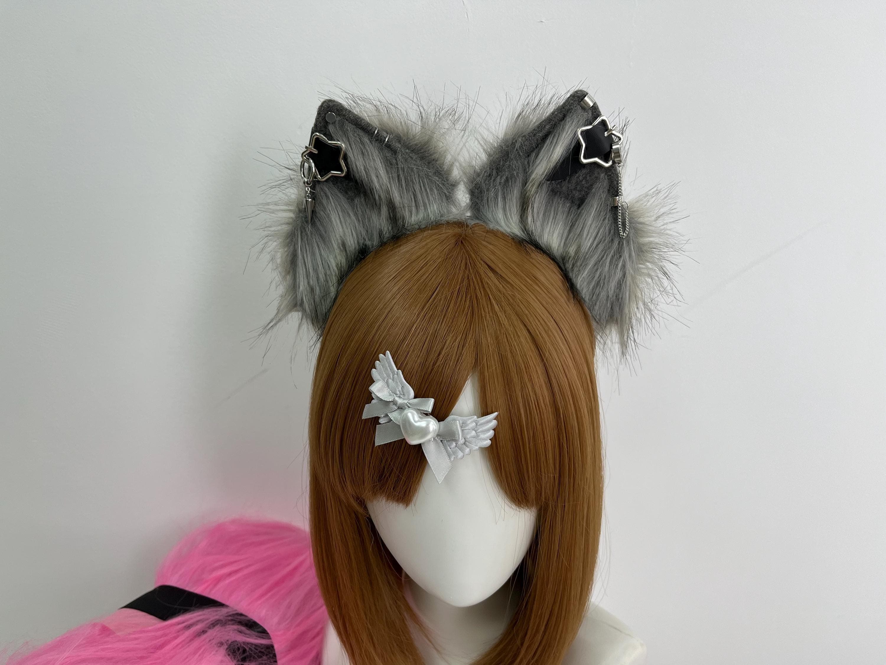 Silver agouti faux fur grey cat ears headband front view showing realistic wolf style two tone fur with black roots pale silver midsection and soft white tips. Left ear features dangling black star charm piercing with silver chain while right ear shows matching star cuff drop. Pointed upright feline ear shape ideal for cosplay convention wear anime costume parties Halloween fantasy outfits therian kin expression gothic cat ears alt fashion aesthetic day looks plus kawaii streetwear fits.