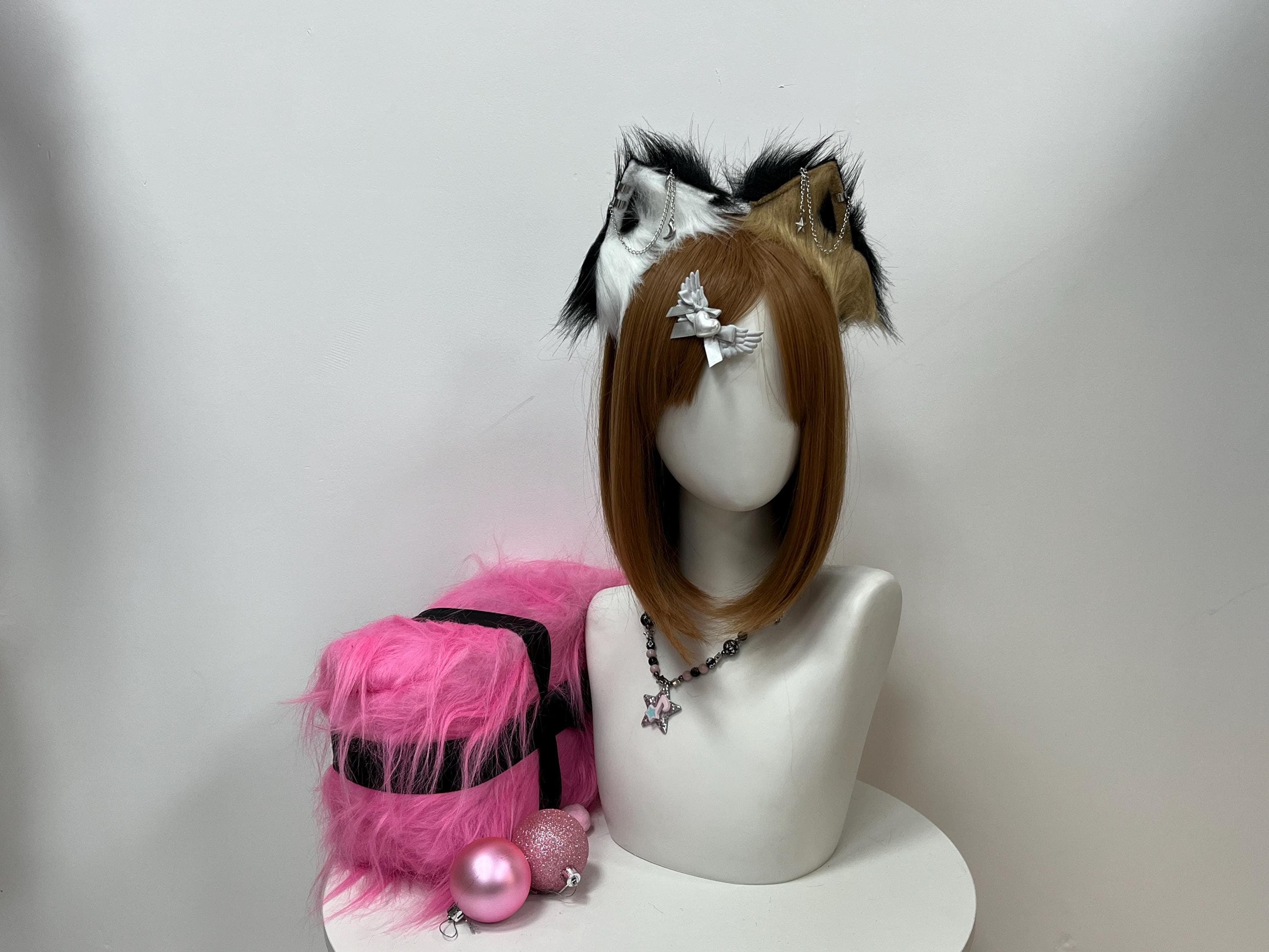 Dual tone realistic wolf ears headband showcased on a styling bust, pairing a snow white ear with bold jet black fur tipping on the left with a warm camel tan and golden brown ear carrying matching inky tipping on the right, both accented by dangling silver chain star and crescent moon piercings. Handcrafted from plush faux fur and sculpted to echo a wild timber wolf pelt, a prime pick for therian debuts, furry con meetups, kemonomimi character builds, and layered Halloween canine fits.