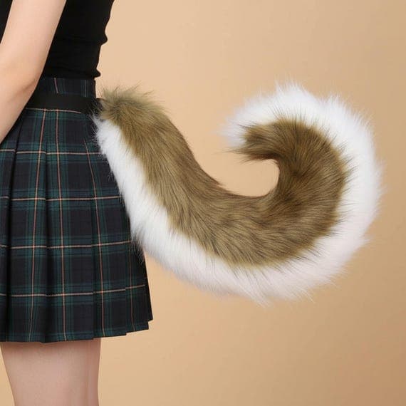 Side view of reddish brown faux fur shiba inu curled tail worn at waist with adjustable belt strap on plaid skirt. Fluffy plush two-tone tail with auburn fur on top and white fur on underside curling into tight spiral shape. Shiba inu dog tail cosplay accessory therian costume prop realistically proportioned against human body showing full 75cm length and 15cm curl diameter. Warm beige studio background.