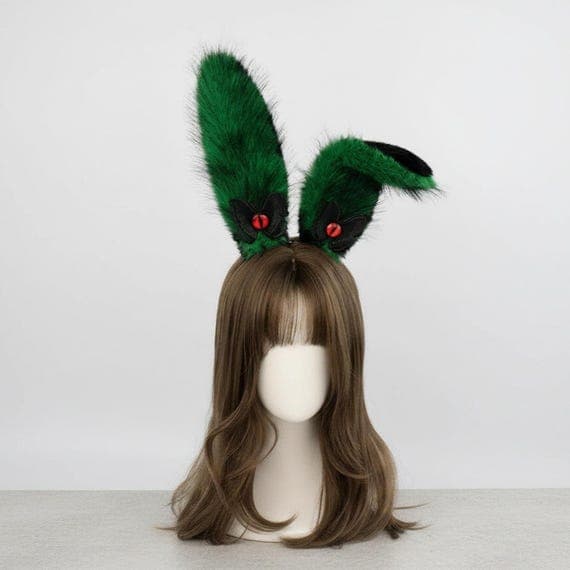 Devil eye bunny ears headband in green and black on mannequin head with styled wig, green plush faux fur rabbit ears with embroidered reptilian devil eye and black wing accent at base, dark fantasy demon style gothic rabbit ear hair accessory great for cosplay costumes anime conventions Halloween parties and goth themed dress-up looks, evil eye bunny ear headpiece perfect for photo shoots festival wear and unique dark costume accessories for women teens and cosplay enthusiasts